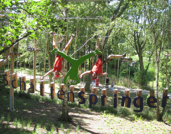 Komm zum Schnupperklettern Zwei Mitarbeiter hängen kopfüber neben einem einem großen Schattenspringerlogo in einem Kletterelement